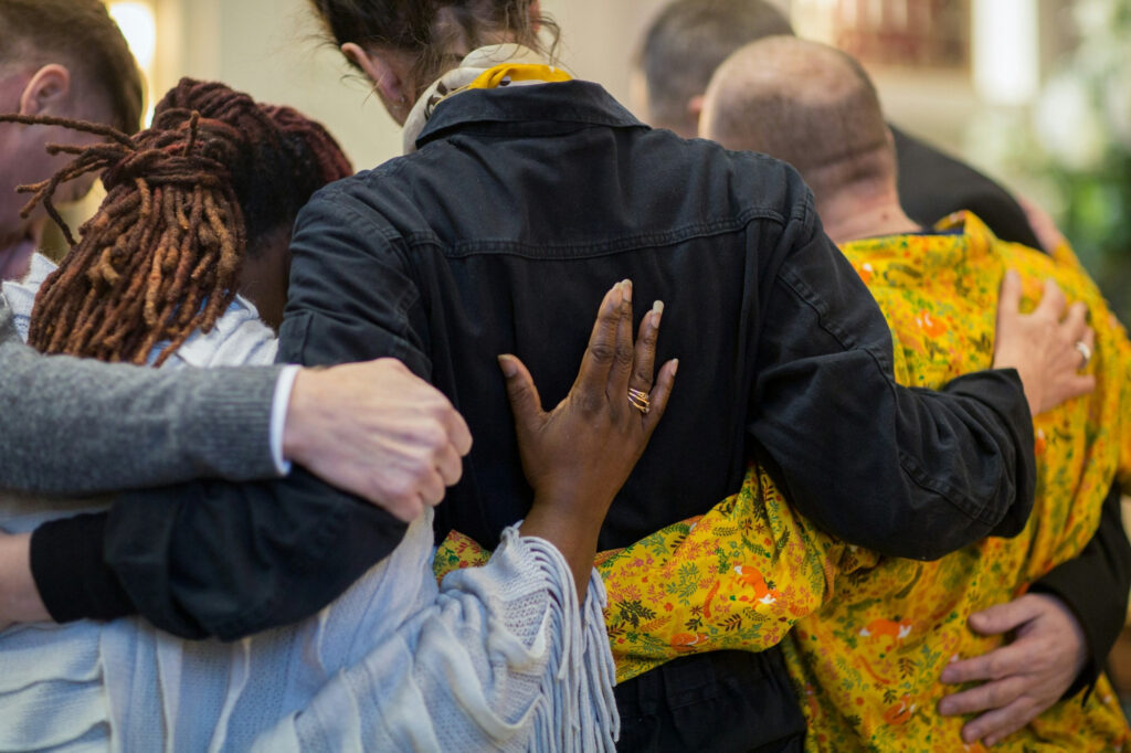 People standing in a huddle with their arms around each other. We see the backs of their heads and the tops of their backs