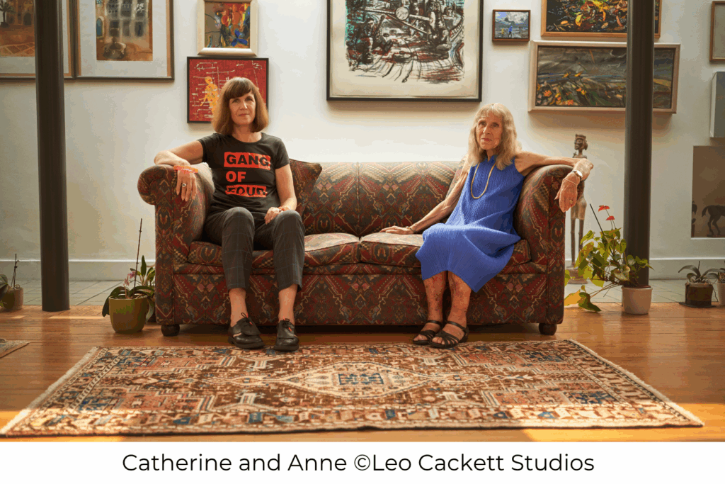 Catherine and Anne sat on a sofa in front of a wall of art. Photo credit: Leo Cackett Studios